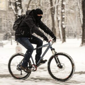 Cyklist i mörka kläder tar sig fram på snötäckt cykelbana